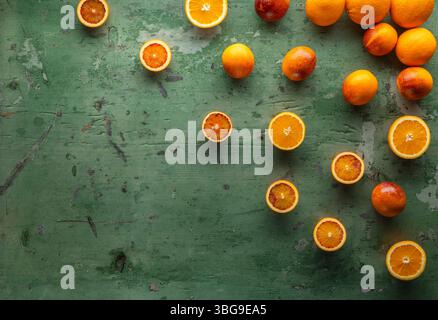 Vibrant arrangement of whole and halved oranges and blood oranges creating a colorful display on a rustic green wooden surface Stock Photo