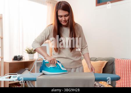 Woman Doing Clothes Housework Ironing Chore Home Household Asian Female Appliance, Lady Smiling While Ironing and Folding Laundry Neatly in a Bright L Stock Photo