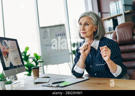 Professional mature woman working in a modern office environment, thoughtful and focused on a project at her desk Stock Photo