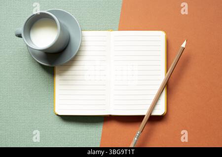 Blank open notebook and pencil, cup of milk on green and red desk background. flat lay, top view, copy space Stock Photo