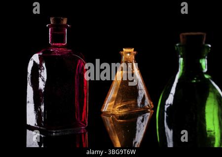 Still life of three coloured decorative bottles with corks on glass against black background Stock Photo