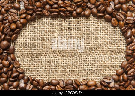 Format-filling view of an oval frame made of roasted coffee beans on sackcloth Stock Photo