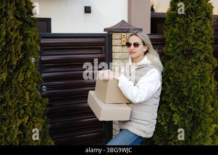 Courier delivering two cardboard boxes in front of a residential house gate, fulfilling ecommerce orders for customers in the neighborhood Stock Photo