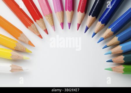 Coloured pencils arranged in a semicircle on white paper, top view Stock Photo