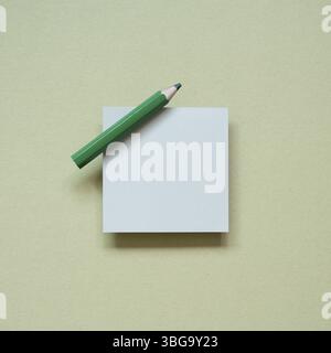 Blank memo pad with green pencil on khaki desk background. top view Stock Photo