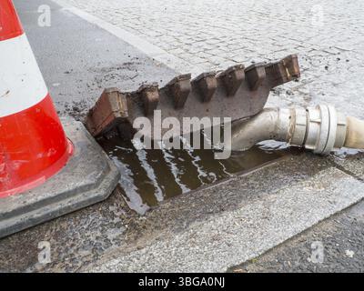 Close-up of an overflowing gully with fire hose and traffic cone on a Berlin street Stock Photo