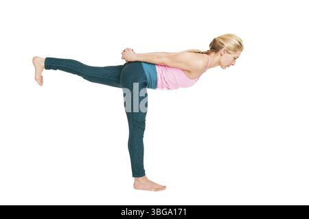 Side full-body view of a young woman performing a variation of the warrior yoga exercise (Virabhadrasana) against a white background with a light shad Stock Photo