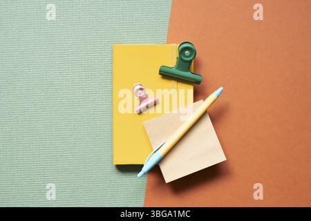 Yellow notebook and pen, clip on green and red desk background. study and workspace. flat lay, top view, copy space Stock Photo