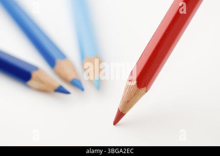 Flat-angled detail view of a red wooden coloured pencil placed diagonally on paper three coloured pencils in blue tones lying flat, the tips turned to Stock Photo