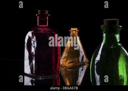 Still life of three coloured decorative bottles with corks on glass against black background Stock Photo