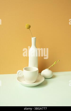 Minimal white ceramic coffee cup and vase of flower on mint green table. orange wall background Stock Photo