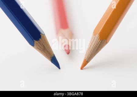 Flat-angled close-up of three wooden coloured pencils in blue, red and yellow arranged in a circle with the tips resting on drawing paper Stock Photo