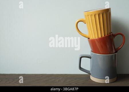 Stack of colorful ceramic mug cups on wooden table. blue wall background Stock Photo