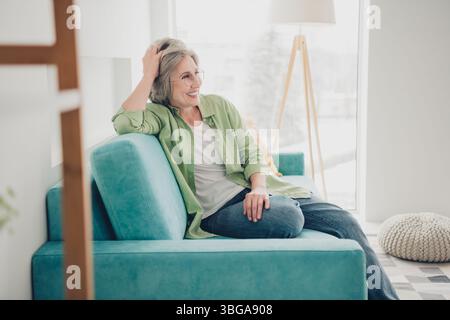 Mature woman with gray hair lounging on a vibrant blue sofa in a modern and cozy living room setting Stock Photo