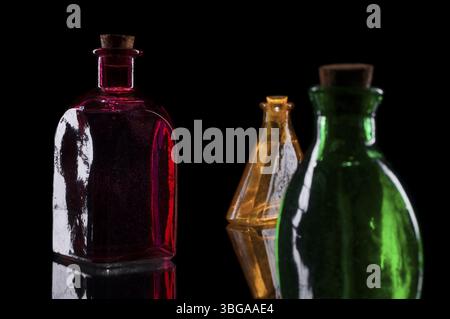 Still life of three coloured decorative bottles with corks on glass against black background Stock Photo