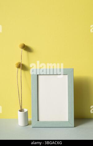 Photo frame with vase of dry flower on gray shelf. yellow wall background Stock Photo