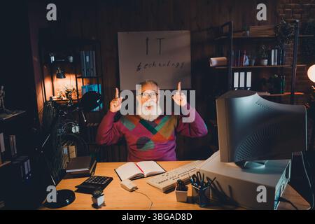 Elderly Bearded Man Enthusiastically Working on Technology Concepts in Cozy Home Office with Dim light During Evening Stock Photo