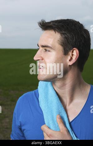 Side head-and-shoulders shot of a young man in a blue T-shirt and blue towel around his neck looking to the side Stock Photo
