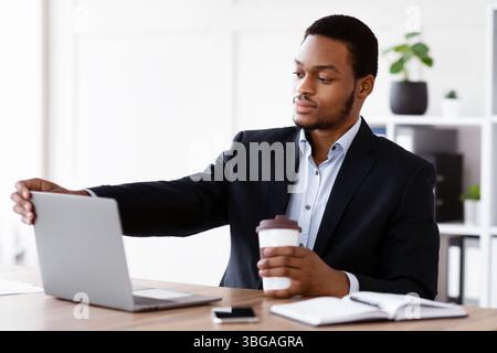 Young black businessman opening his notebook, drinking coffee, office interior Stock Photo
