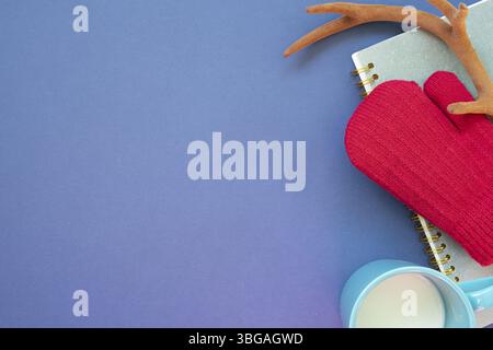 Winter knitted red gloves, antler, notebook, cup of milk on navy blue background. top view, copy space Stock Photo