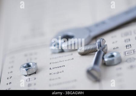 Detailed view of a small open-end spanner with bolts and nuts in front of it on the page of an old table book Stock Photo