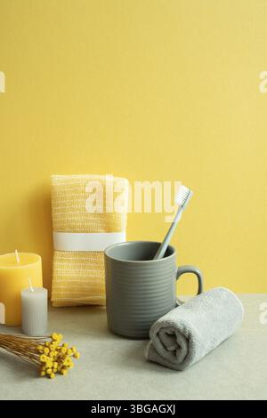 Bathroom shower towel and toothbrush, cup, candle, dry flower on gray table. yellow background Stock Photo