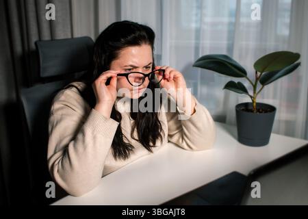 Female with bad eyesight trying to read information from computer using eyeglasses. Freelancer using laptop for work. Stock Photo