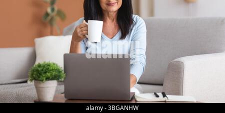 Mature woman holding coffe cup and working on computer Stock Photo