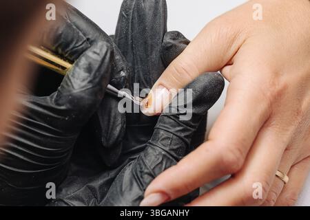 Manicure in progress with black gloves. Nail polish application by beauty professional. Closeup of brush painting fingernails. Hand care and beauty. Stock Photo