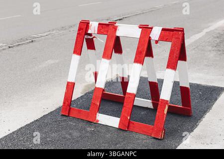 Red and white road barrier. Street obstacle for traffic safety. Construction zone blocking passage. Urban repair site with asphalt surface. Stock Photo