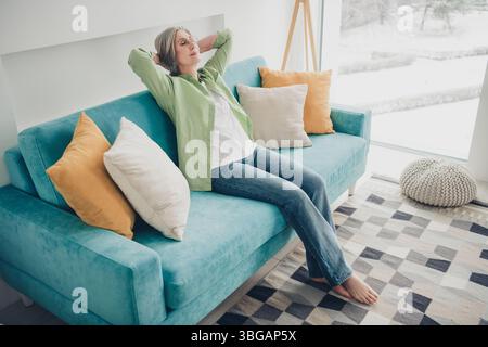 Middle aged woman reclining on a modern sofa enjoying a serene moment in a cozy living room with bright ambience Stock Photo