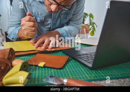 Latin craftsman working with leather at his workshop, using a laptop and tools for his small business Stock Photo