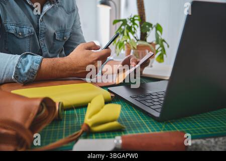 Leather craftsman using smartphone and credit card for online shopping in his workshop Stock Photo
