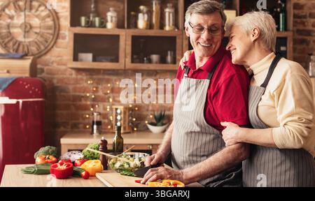 Cheerful senior woman hugging her husband back at kitchen Stock Photo