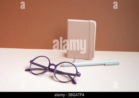 Diary notebook, pen, eyeglasses on pink desk. red background Stock Photo