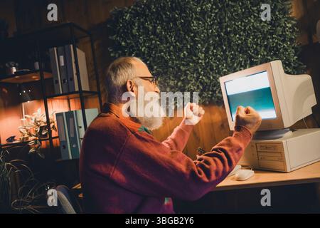 Enthusiastic elderly man engaging with technology, showcasing programming and coding skills on a vintage computer setup Stock Photo