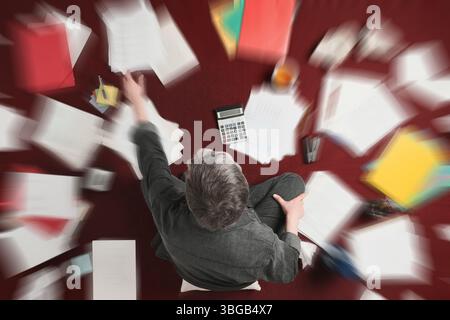 Accounting and processing a mess of stressful paperwork. Man doing challenging work with taxes, overhead shot with zoom blur effect Stock Photo