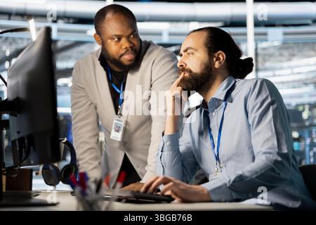 Data center manager supervising work done by employee verifying neural network parameters. Server hub supervisor overseeing worker inspecting configurations to ensure optimal performance Stock Photo
