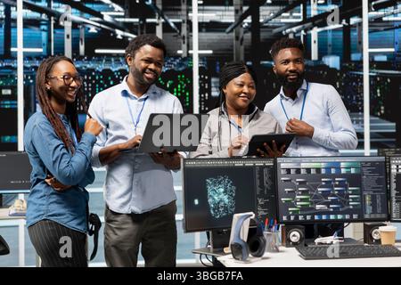 Cheerful data center experts working together, using deep learning algorithms and node trees to analyze datasets. Jolly server farm teamworking colleagues using AI to recognize facility data patterns Stock Photo