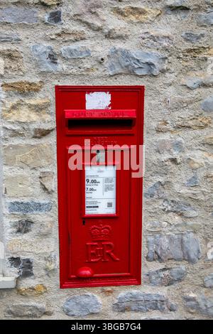 Red British Royal Mail postbox mounted on a stone wall with ER insignia and collection times displayed Stock Photo