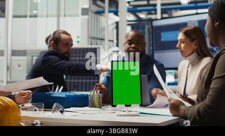 Photovoltaics plant specialists design solar cell prototypes on mockup device. Factory engineers using isolated screen tablet to refine designs for increased energy output using data, camera A Stock Photo