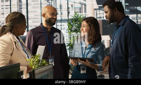 Relaxed multiethnic coworkers in office having fun chatting while reviewing documents, analyzing metrics. Smiling multiracial colleagues talking, working together, looking over paperwork, camera A Stock Photo