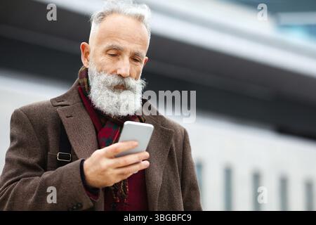 Grey-haired businessman using smartphone on the street Stock Photo