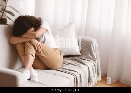 Depressed brunette woman sitting on couch alone, crying Stock Photo