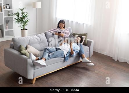 High angle view relaxed eastern lovers using gadgets at home Stock Photo