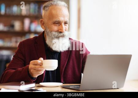 Positive senior man drinking coffee and using laptop Stock Photo