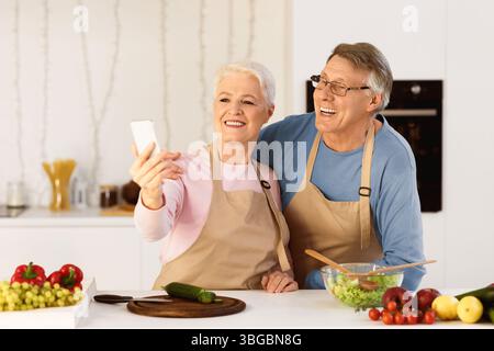 Joyful Elderly Spouses Making Selfie Having Fun Cooking In Kitchen Stock Photo