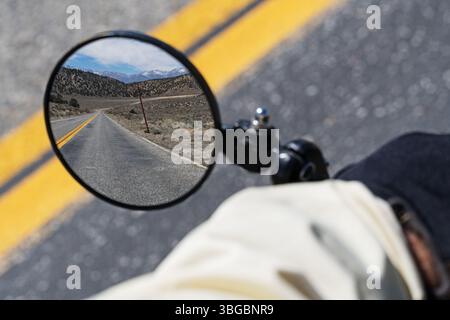 round bicycle mirror showing an empty road behind with an out of focus hand and arm and road Stock Photo