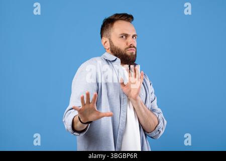 Repulsed millennial guy rejecting something, making STOP gesture over blue studio background Stock Photo