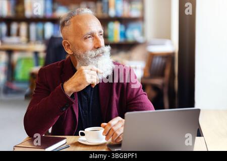 Thoughtful senior man sitting at cafe, using laptop Stock Photo